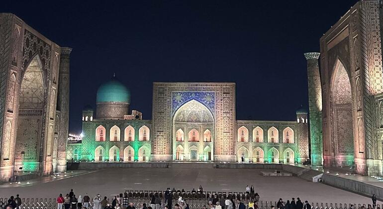 Illuminated historic Registan square in Samarkand at night with crowds gathered in the plaza.